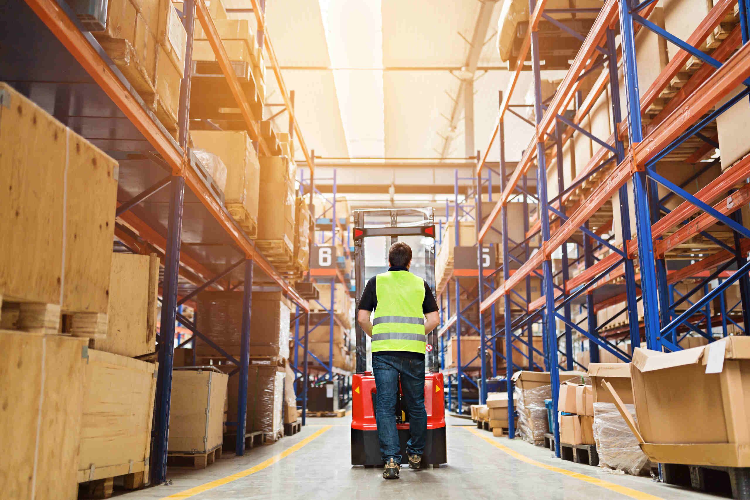 Storehouse employee in uniform working on forklift in modern warehouse.