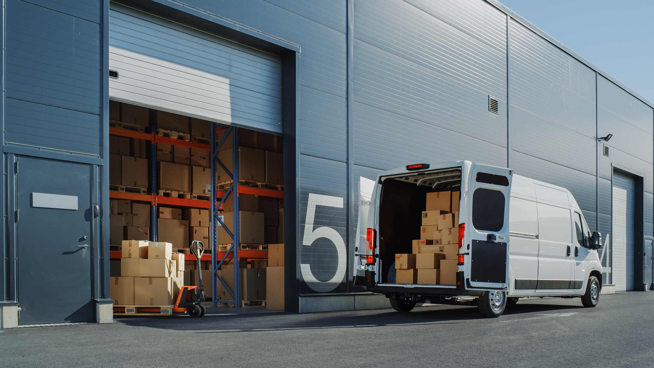 Outside of Logistics Warehouse with Open Door, Delivery Van Loaded with Cardboard Boxes